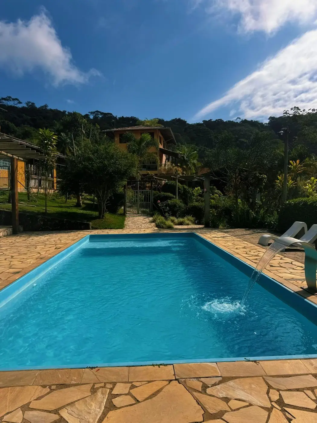 Piscina do sítio com espreguiçadeiras e a mata ao fundo